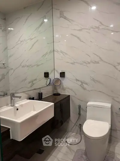Modern bathroom with sleek fixtures and marble walls, featuring a stylish sink and toilet.