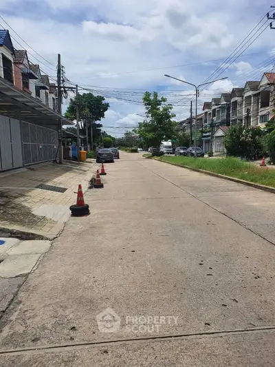 Charming residential street with townhouses and lush greenery under a clear sky.