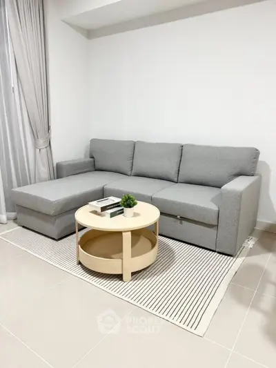 Modern living room with stylish gray sofa and round wooden coffee table on a striped rug.