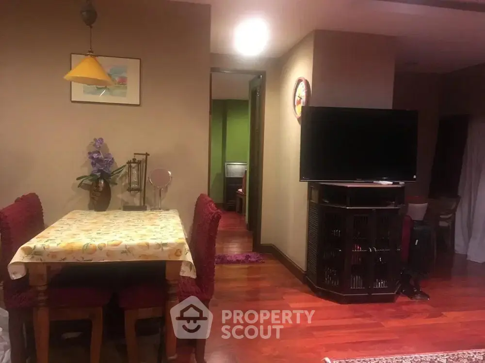 Cozy living room with wooden flooring and dining area, featuring a TV and elegant decor.