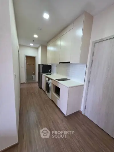 Modern kitchen with sleek cabinetry, washing machine, and built-in oven in a compact layout.