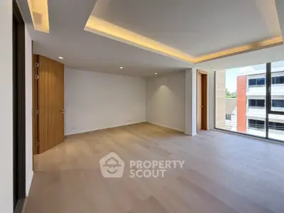 Spacious modern living room with wooden flooring and large windows offering natural light.