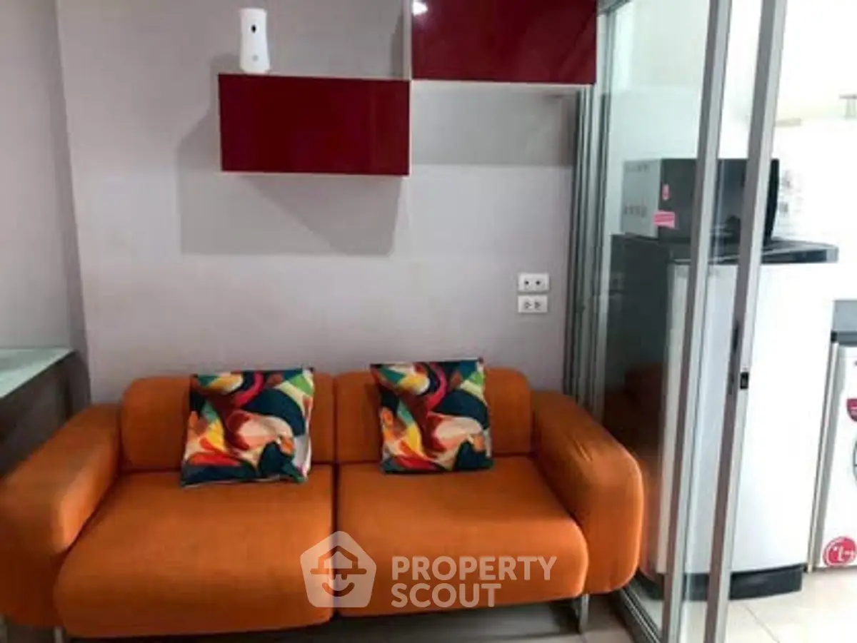 Modern living room with vibrant orange sofa and colorful cushions, adjacent to a sleek kitchen area.