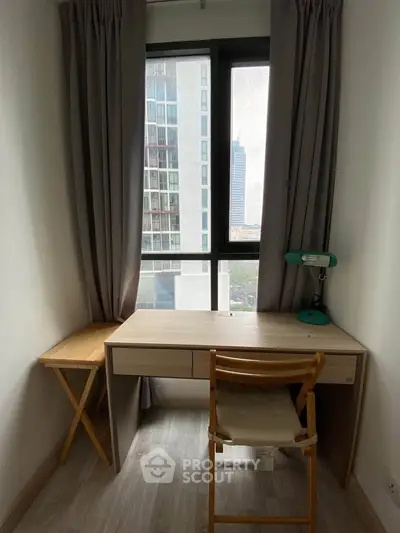 Cozy study nook with desk and chair, offering a city view through large window.