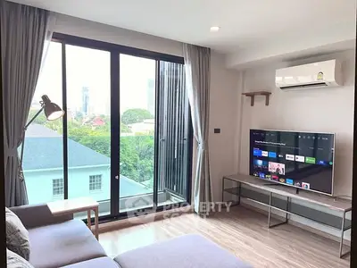 Modern living room with large windows and city view, featuring a sleek TV setup.