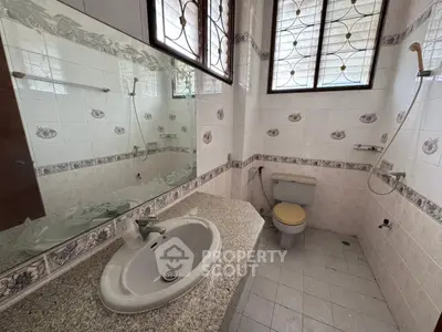Spacious bathroom with large mirror and tiled walls, featuring a sink and toilet.