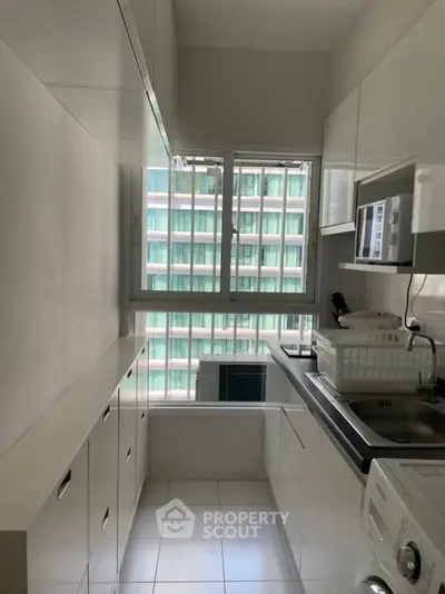 Modern compact kitchen with sleek white cabinets and large window view.