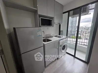 Modern compact kitchen with balcony view, featuring fridge, microwave, and washing machine.