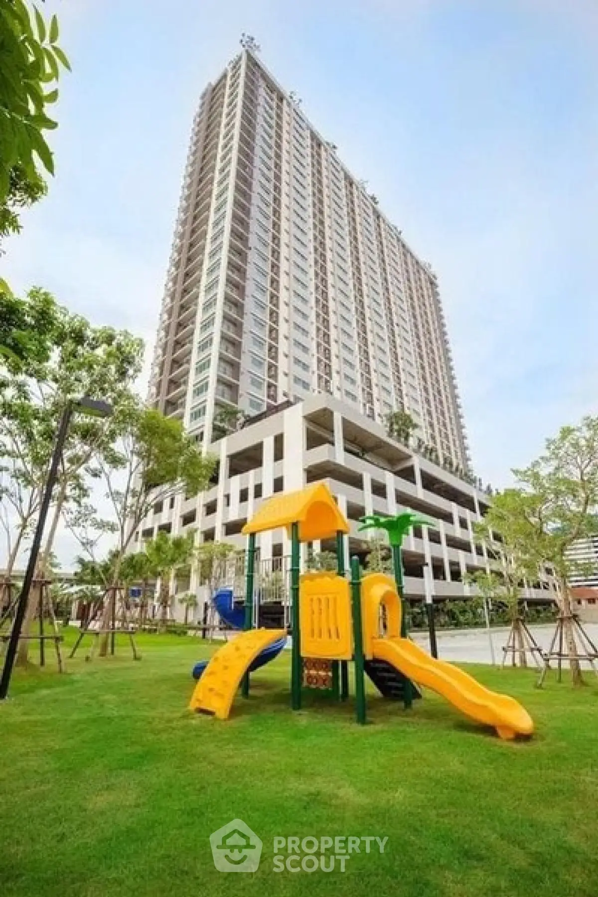 Modern high-rise building with lush green lawn and children's playground.