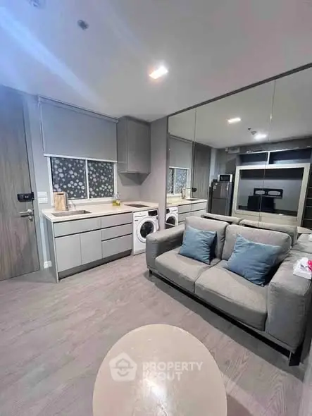 Modern living room with integrated kitchen and washing machine, featuring sleek design and cozy seating.