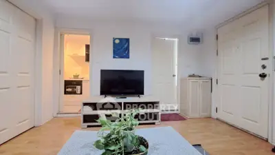 Cozy living room with TV and plant, adjacent to kitchen and entrance
