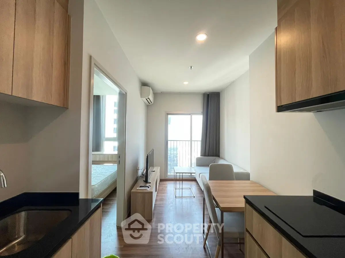 Modern apartment interior with open kitchen and cozy living area, featuring sleek wooden cabinetry and natural light.