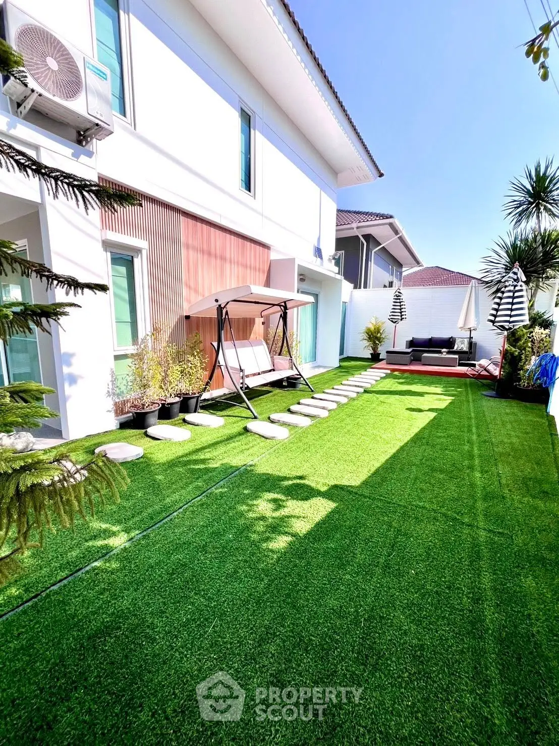 Modern house exterior with lush green lawn and stylish outdoor seating area.