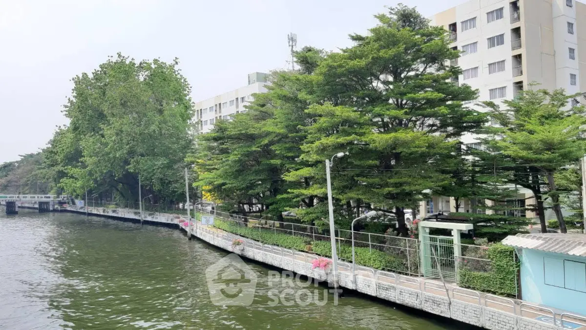 Scenic riverside view of modern apartment building with lush greenery and serene walkway.