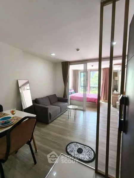 Modern open-plan living room with cozy sofa and dining area, leading to a bright bedroom.