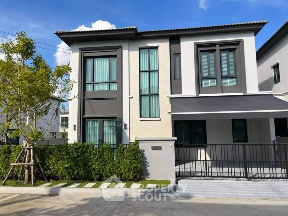 Modern two-story house with sleek design and large windows, surrounded by greenery and a paved driveway.