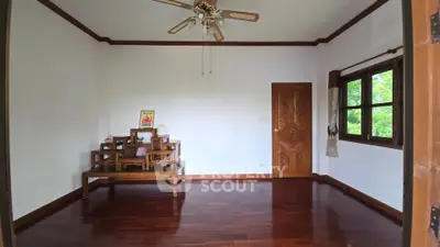 Spacious living room with wooden flooring and elegant furniture, featuring a ceiling fan and large windows for natural light.