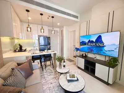 Modern living room with open kitchen, stylish decor, and large TV display.