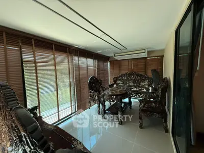 Luxurious living room with ornate wooden furniture and large windows with blinds.