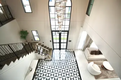 Luxurious modern living room with high ceilings and elegant staircase, featuring large windows and stylish decor.