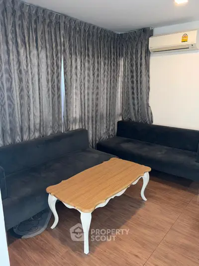 Cozy living room with elegant wooden table and stylish black sofas, complemented by chic curtains and modern air conditioning.