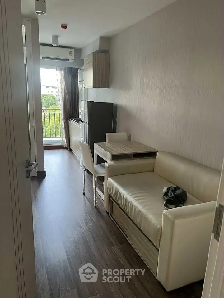 Modern apartment interior with compact living area and balcony view, featuring sleek furniture and wooden flooring.