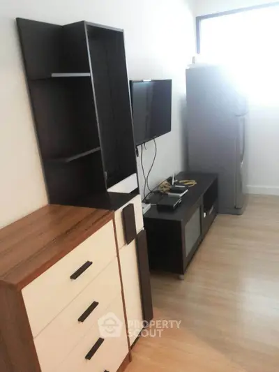 Modern apartment interior with sleek furniture and appliances, featuring a TV and refrigerator.