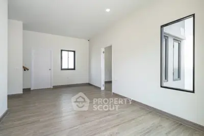 Spacious empty room with wooden flooring and large window, ideal for customization.