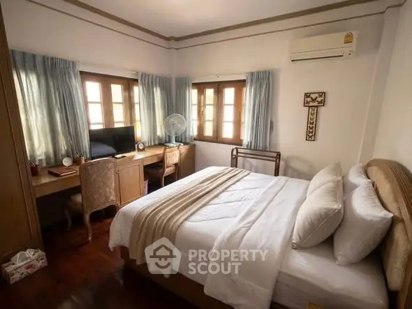 Charming bedroom with wooden accents, cozy bed, and natural light from multiple windows.
