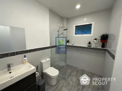 Modern bathroom with sleek design, featuring a glass shower, stylish tiling, and a well-lit vanity area for a refreshing ambiance.