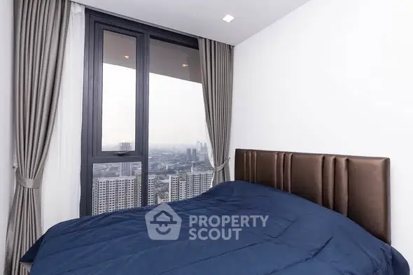 Modern bedroom with stunning city view from large window, featuring elegant curtains and cozy bedding.