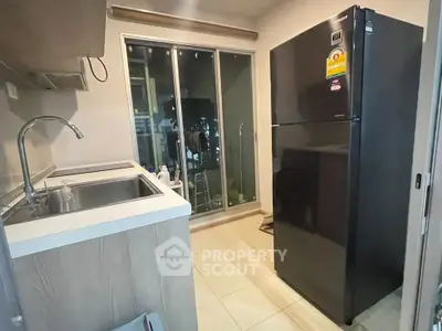 Modern kitchen with sleek black fridge and sliding glass doors leading to balcony.