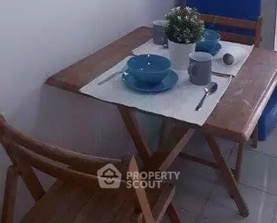 Cozy dining nook with wooden table and chairs, set for two with blue dishware and a potted plant centerpiece.