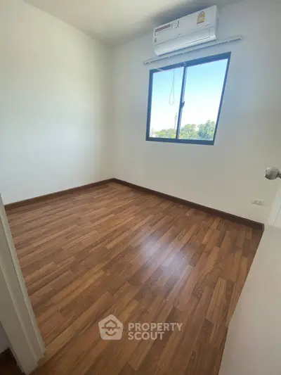 Spacious bedroom with wooden flooring and natural light from window.