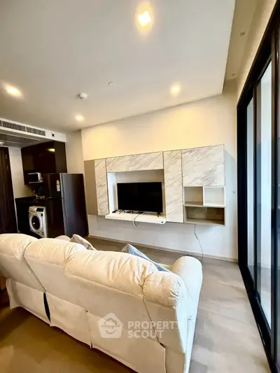 Modern living room with sleek entertainment center and cozy sofa, featuring a compact kitchen area with appliances.