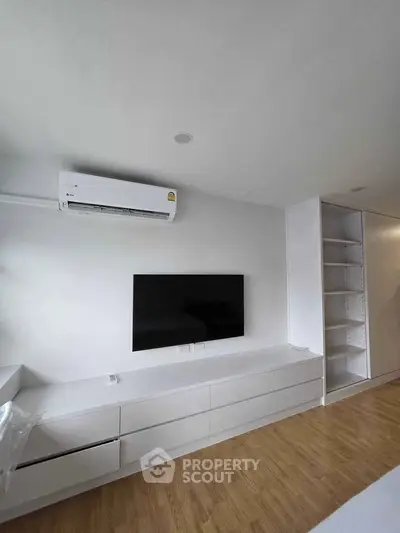 Modern living room with sleek white cabinetry and wall-mounted TV, featuring minimalist design and wooden flooring.