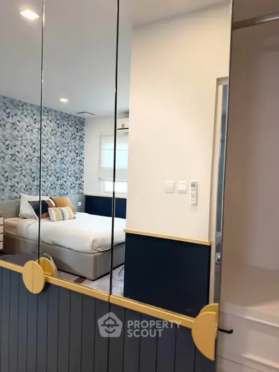 Modern bedroom with stylish decor and mirrored wardrobe doors, featuring a cozy bed and patterned accent wall.