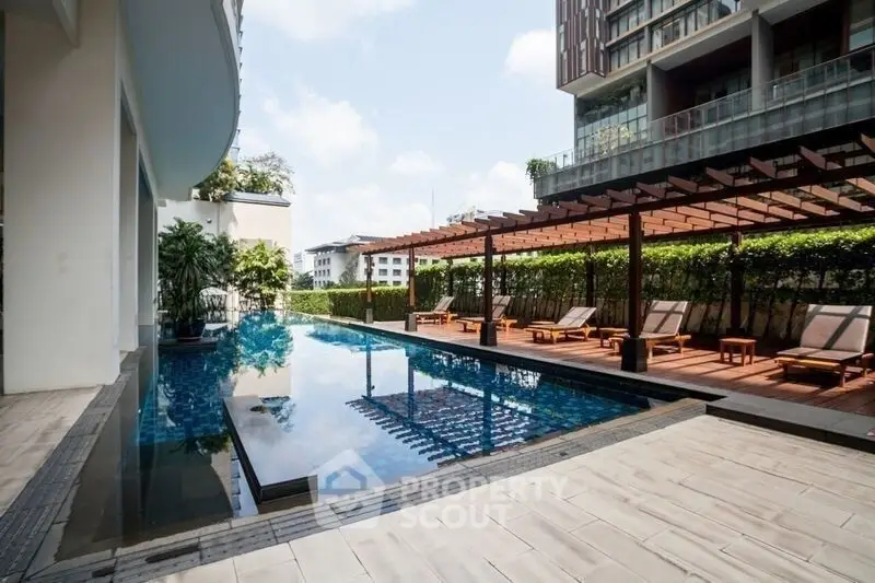 Luxurious modern apartment pool with sun loungers and pergola, perfect for relaxation and leisure.