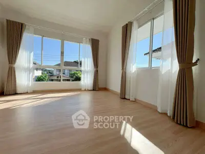 Spacious sunlit room with large windows and elegant curtains, perfect for a cozy living space.
