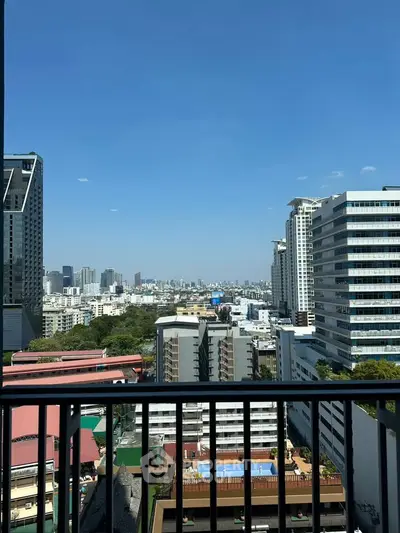 Stunning cityscape view from a high-rise balcony showcasing urban skyline and clear blue skies.