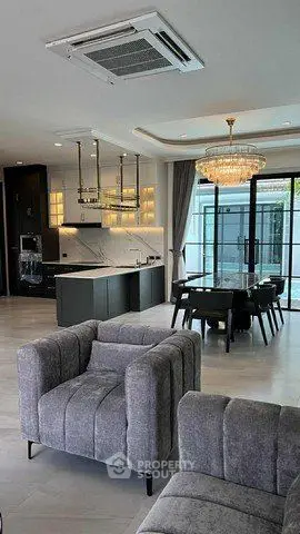 Luxurious open-plan living room with modern kitchen and elegant dining area, featuring stylish gray furniture and a chic chandelier.