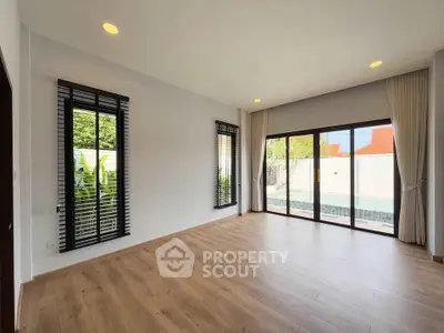 Spacious living room with large windows and pool view, featuring elegant wooden flooring.