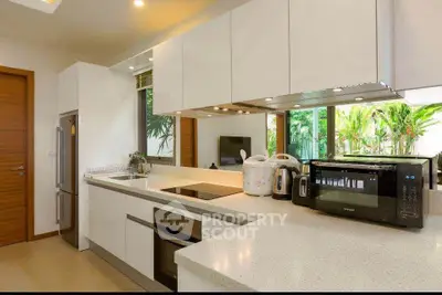 Modern kitchen with sleek white cabinetry and appliances, featuring a large window view of lush greenery.