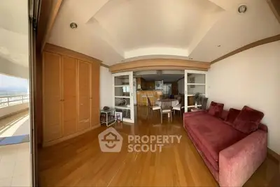 Spacious living room with wooden floors and red sofa, adjacent to open kitchen and balcony.