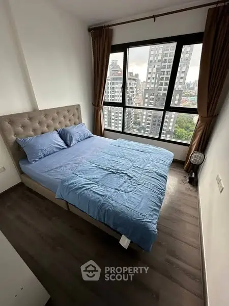 Cozy bedroom with large window offering stunning city view, featuring modern decor and wooden flooring.