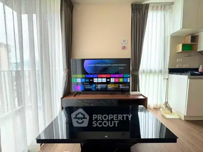 Modern living room with sleek TV setup and open kitchen layout, featuring large windows and stylish decor.