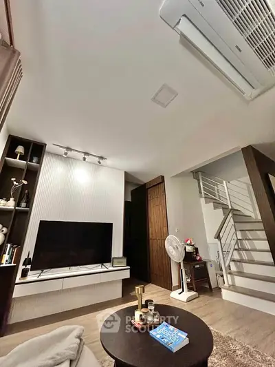 Modern living room with stylish decor and staircase, featuring a sleek TV setup and cozy ambiance.