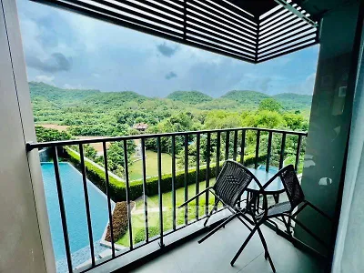 Stunning balcony view overlooking lush green hills and serene pool area.