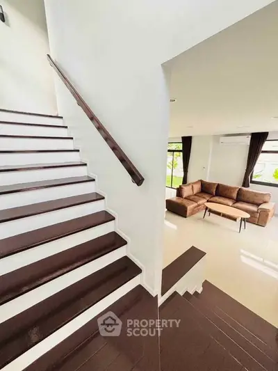 Modern staircase leading to a cozy living room with stylish brown sofa and large windows.
