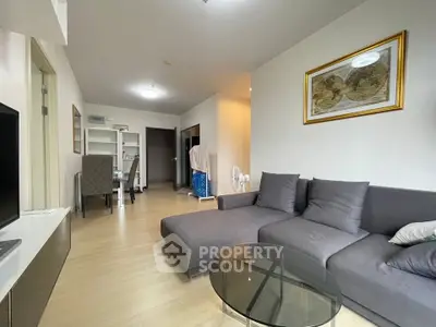 Modern living room with gray sectional sofa and glass coffee table in cozy apartment.